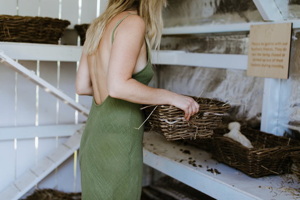 Side view of crop unrecognizable female in sundress with straw basket near chicken in hen house