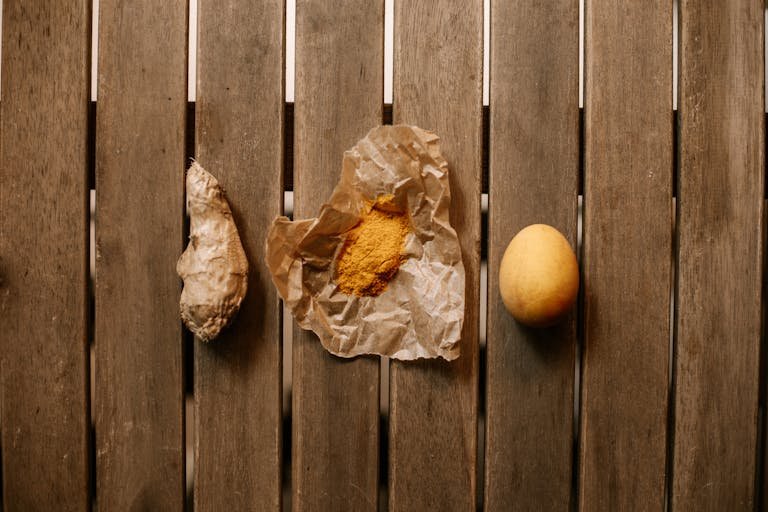 Raw Turmeric, Turmeric Powder and a Chicken Egg Lying on a Wooden Table