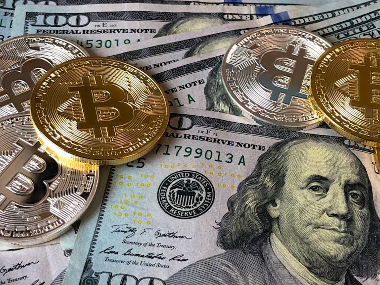 A close-up photo depicting Bitcoin coins on top of US dollar bills, symbolizing finance and cryptocurrency.