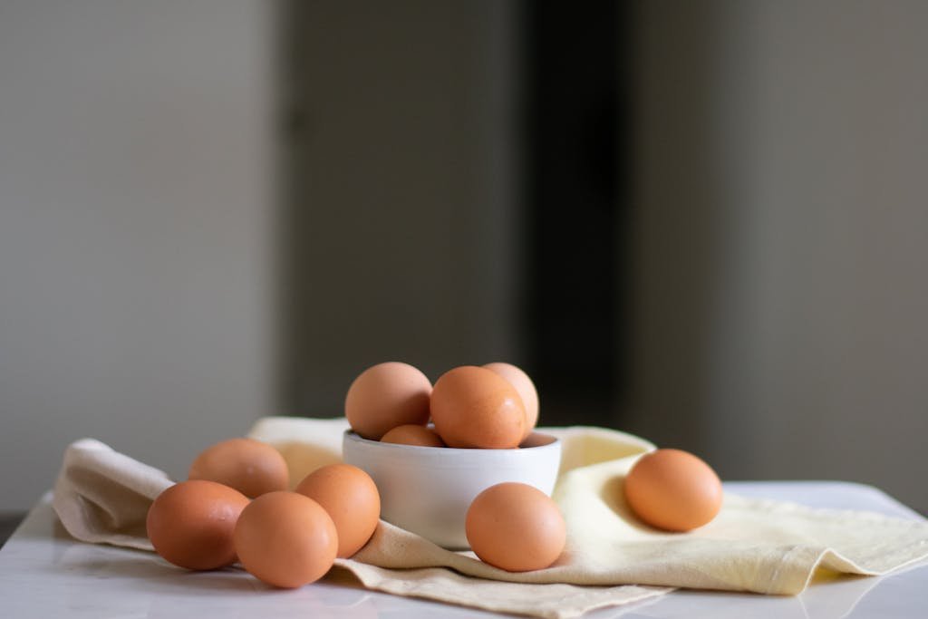 Still life of organic brown eggs in a ceramic bowl on a neutral cloth, showcasing natural textures and a rustic feel.