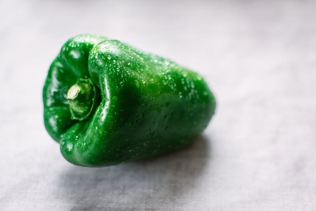 Close-up of a fresh green bell pepper with water droplets, highlighting its vibrant color and freshness