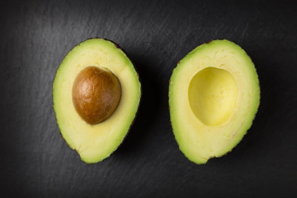 Close-up of fresh sliced avocado halves on a dark slate surface, showcasing healthy eating.