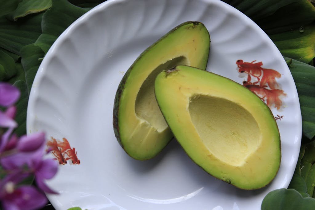 Close-up of sliced avocado on a white plate with floral design, showcasing freshness.