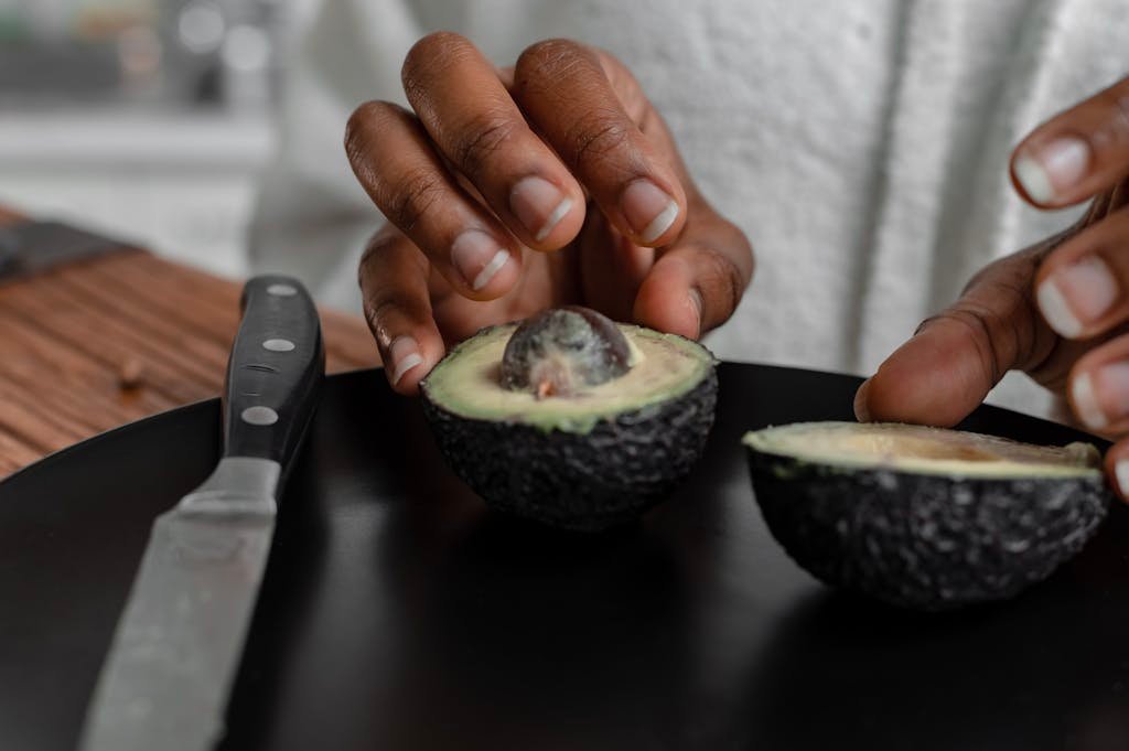 Hands slicing a fresh avocado on a black plate. Ideal for food blogs.